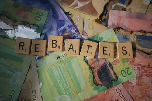 Wooden tiles spelling out "REBATES" sit on top of a pile of Canadian money. This is a demonstration of the money you can get back with personal taxes done froman expert.